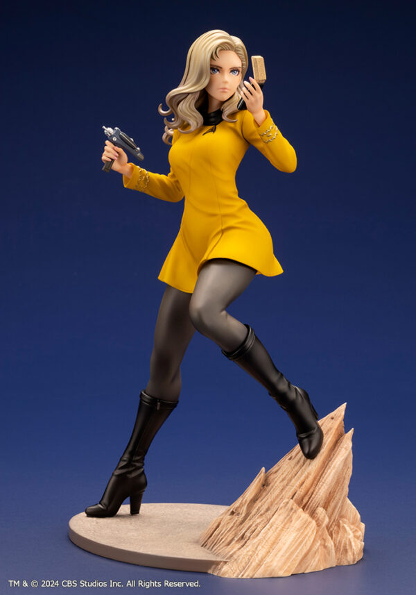 Bishoujo statue of a Star Trek: The Original Series Command Officer, depicted in a dynamic pose holding a phaser and communicator. The character wears a yellow command uniform dress, black boots, and stands on a rocky base. The figure features a stylized design with long flowing blonde hair, capturing the essence of the iconic science fiction series.