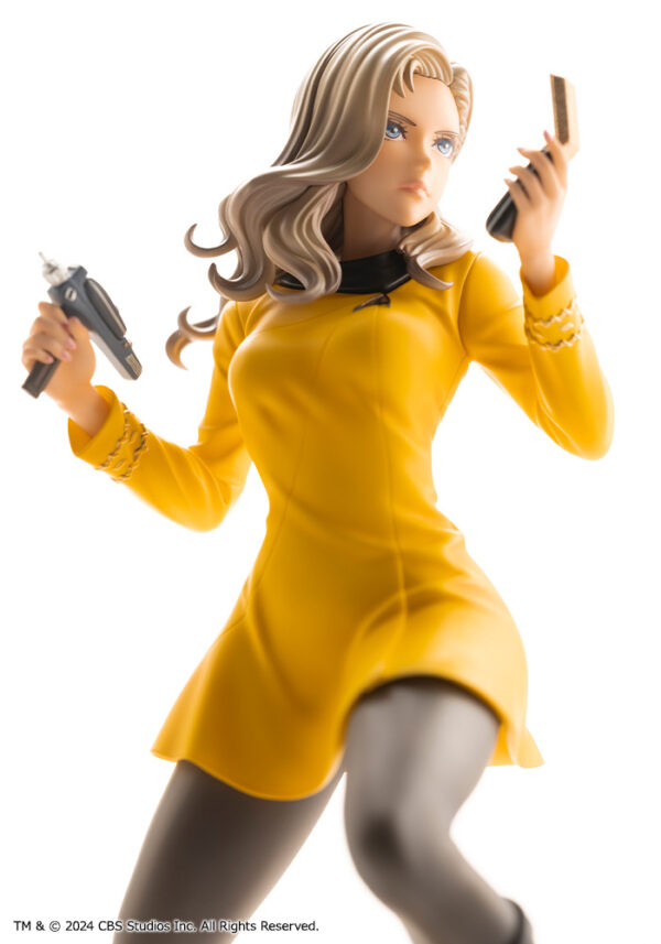 Bishoujo statue of a Star Trek: The Original Series Command Officer, depicted in a dynamic pose holding a phaser and communicator. The character wears a yellow command uniform dress, black boots, and stands on a rocky base. The figure features a stylized design with long flowing blonde hair, capturing the essence of the iconic science fiction series.