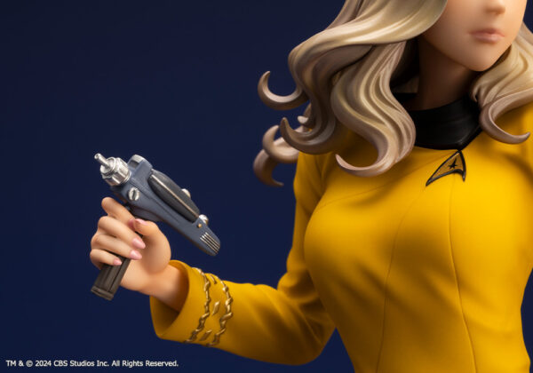 Bishoujo statue of a Star Trek: The Original Series Command Officer, depicted in a dynamic pose holding a phaser and communicator. The character wears a yellow command uniform dress, black boots, and stands on a rocky base. The figure features a stylized design with long flowing blonde hair, capturing the essence of the iconic science fiction series.