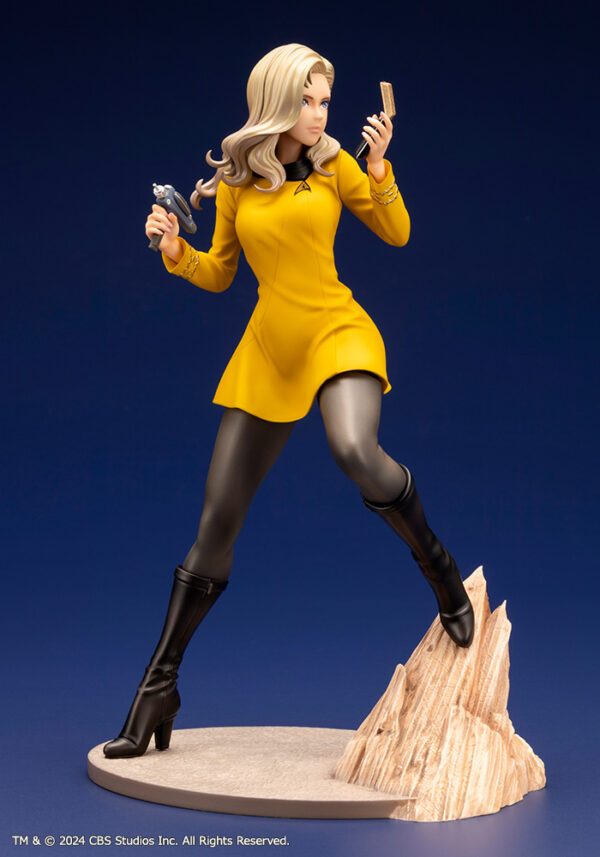 Bishoujo statue of a Star Trek: The Original Series Command Officer, depicted in a dynamic pose holding a phaser and communicator. The character wears a yellow command uniform dress, black boots, and stands on a rocky base. The figure features a stylized design with long flowing blonde hair, capturing the essence of the iconic science fiction series.