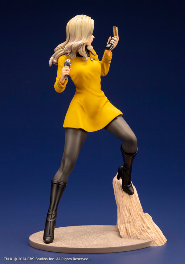 Bishoujo statue of a Star Trek: The Original Series Command Officer, depicted in a dynamic pose holding a phaser and communicator. The character wears a yellow command uniform dress, black boots, and stands on a rocky base. The figure features a stylized design with long flowing blonde hair, capturing the essence of the iconic science fiction series.