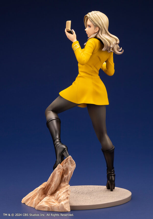 Bishoujo statue of a Star Trek: The Original Series Command Officer, depicted in a dynamic pose holding a phaser and communicator. The character wears a yellow command uniform dress, black boots, and stands on a rocky base. The figure features a stylized design with long flowing blonde hair, capturing the essence of the iconic science fiction series.