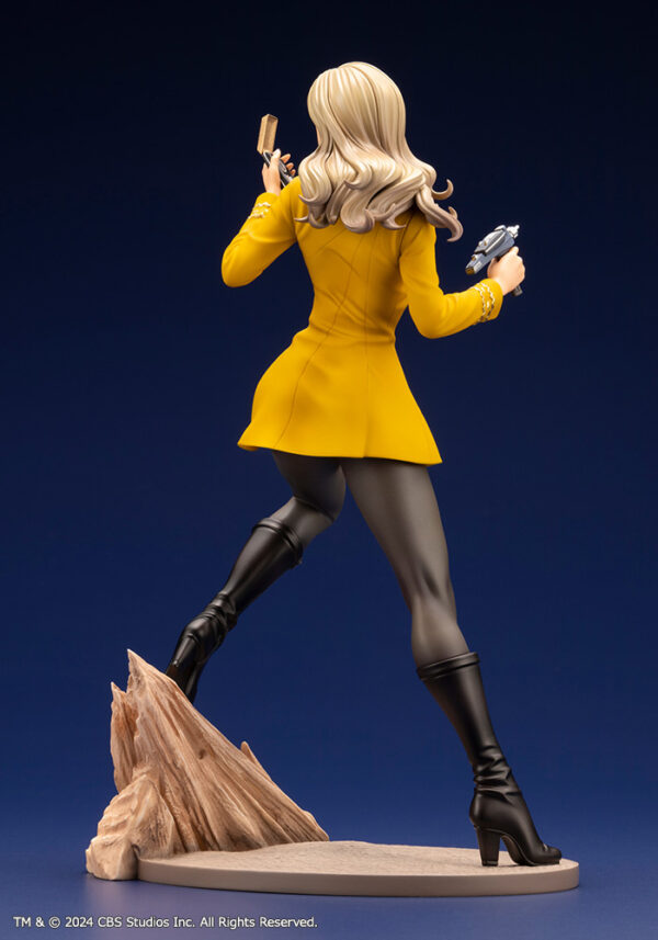 Bishoujo statue of a Star Trek: The Original Series Command Officer, depicted in a dynamic pose holding a phaser and communicator. The character wears a yellow command uniform dress, black boots, and stands on a rocky base. The figure features a stylized design with long flowing blonde hair, capturing the essence of the iconic science fiction series.