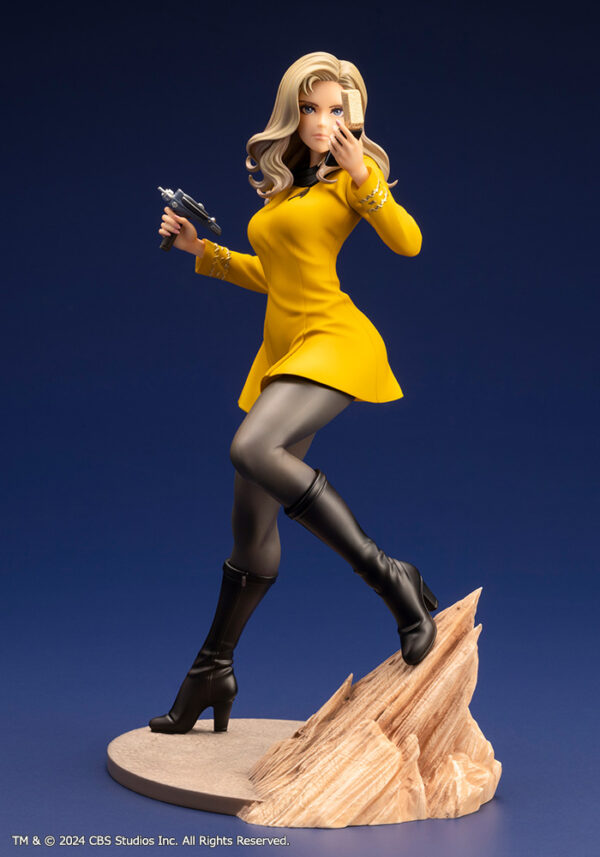 Bishoujo statue of a Star Trek: The Original Series Command Officer, depicted in a dynamic pose holding a phaser and communicator. The character wears a yellow command uniform dress, black boots, and stands on a rocky base. The figure features a stylized design with long flowing blonde hair, capturing the essence of the iconic science fiction series.