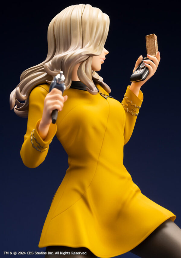 Bishoujo statue of a Star Trek: The Original Series Command Officer, depicted in a dynamic pose holding a phaser and communicator. The character wears a yellow command uniform dress, black boots, and stands on a rocky base. The figure features a stylized design with long flowing blonde hair, capturing the essence of the iconic science fiction series.