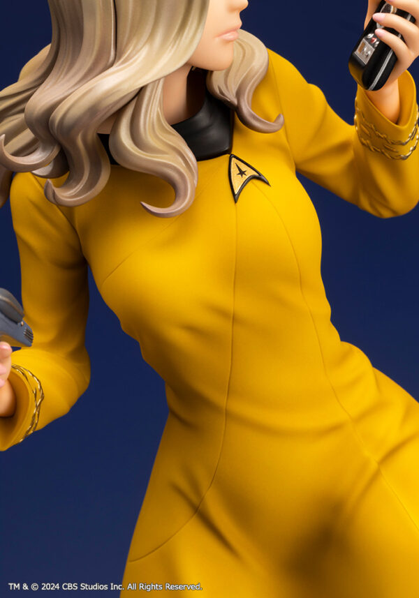 Bishoujo statue of a Star Trek: The Original Series Command Officer, depicted in a dynamic pose holding a phaser and communicator. The character wears a yellow command uniform dress, black boots, and stands on a rocky base. The figure features a stylized design with long flowing blonde hair, capturing the essence of the iconic science fiction series.