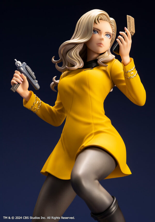 Bishoujo statue of a Star Trek: The Original Series Command Officer, depicted in a dynamic pose holding a phaser and communicator. The character wears a yellow command uniform dress, black boots, and stands on a rocky base. The figure features a stylized design with long flowing blonde hair, capturing the essence of the iconic science fiction series.